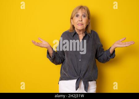 Ältere hübsche Frau, die sich ratlos und verwirrt fühlt, isoliert auf gelbem Hintergrund. Stockfoto