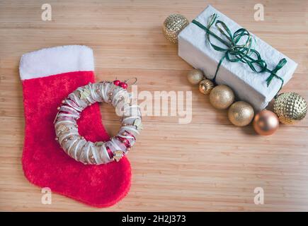 Rote Socke für Weihnachtsgeschenke, Geschenk auf recyceltem Papier verpackt, goldene Kugeln Dekorationen auf dem Tisch. Stockfoto