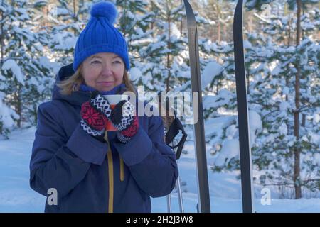 Porträt einer lächelnden älteren Frau, die nach der Outdoor-Aktivität im Winterwald am verschneiten Wintertag Tee trinkt. Aktiver Lebensstil im höheren Alter Stockfoto