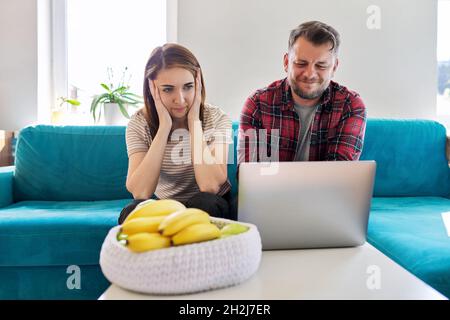 Ernsthaftes Paar mittleren Alters, das zu Hause im Wohnzimmer einen Laptop-Bildschirm ansieht Stockfoto