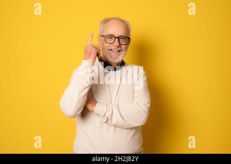 Glücklicher älterer Mann zeigt den Finger isoliert auf gelben Hintergrund. Stockfoto