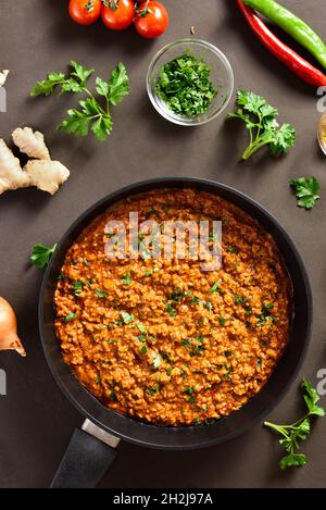 Keema Curry in Bratpfanne über dunklem Hintergrund. Indische und pakistanische Gerichte. Draufsicht, flach liegend, Nahaufnahme Stockfoto