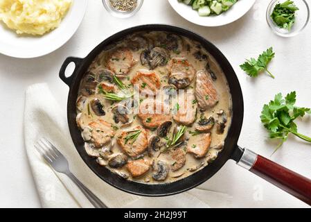 Schweinemedaillons mit Pilzsauce in gusseiserner Pfanne auf weißem Steingrund. Draufsicht, flach liegend Stockfoto