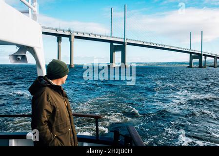 Ein Mann-Tourist mit Blick auf das Meer auf einer Bootsfahrt auf dem Muray firth in inverness mit der Kessock-Brücke im Hintergrund Stockfoto