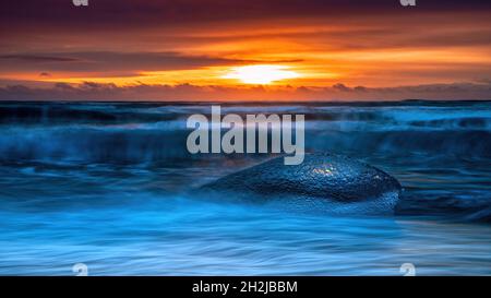 Eisbrocken auf dem schwarzen Sand von Diamond Beach. Eis wird am Strand von der nahe gelegenen Jokulsarlon Gletscherlagune abgelagert. Sonnenaufgang in Island. Stockfoto