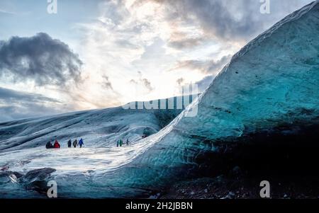 Touristen machen sich auf den Weg über einen Gletscher, um Eishöhlen in Island zu besuchen. Die Höhlen sind in Blautönen gefärbt und haben oft Schichten von schwarzer, Form Stockfoto