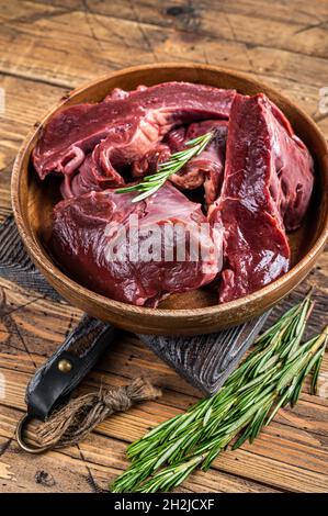 Geschnittenes Rindfleisch oder Kalbfleisch rohes Herz in einem Holzteller mit Kräutern. Holzhintergrund. Draufsicht Stockfoto