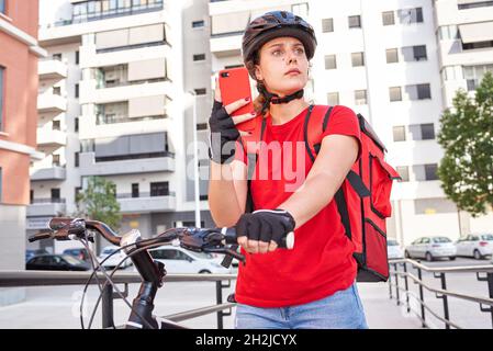 Eine Radfahrerin überprüft die Adresse ihrer nächsten Lieferung mit ihrem Mobiltelefon Stockfoto