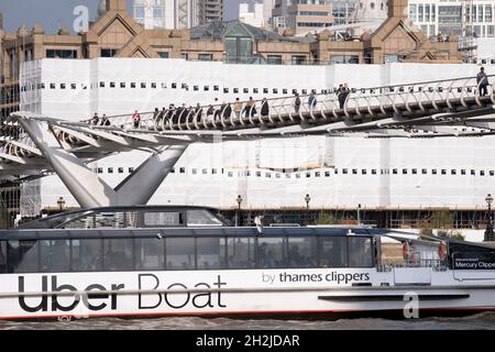 Der „Meteor Clipper“ von Uber Boat führt unter der Millennium Bridge vorbei an Firmenimmobilien, die am 19. Oktober 2021 in London, England, renoviert wurden und die Themse überblicken. Thames Clippers betreibt eine Flotte von 20 Booten auf der Themse, die von 23 Piers quer durch London von Putney nach Woolwich abfährt. Stockfoto