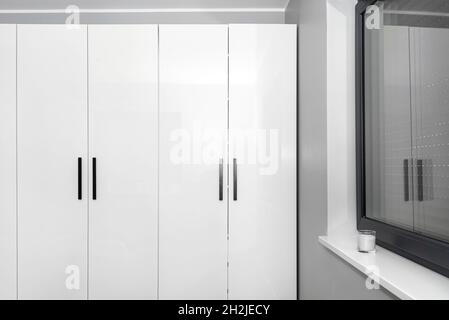 Großer und hoher Kleiderschrank im Schlafzimmer mit weißen Fronten und schwarzen Griffen. Stockfoto