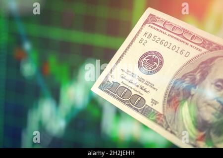 Hand hält Dollar Banknote auf grünen Aktiendiagramm Finanzgraphen Hintergrund. Wirtschaftswachstum, Währungswechselkonzept Stockfoto