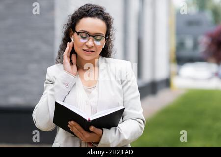 afroamerikanische Geschäftsfrau, die im Freien in einem Notebook den Kopfhörer berührt Stockfoto