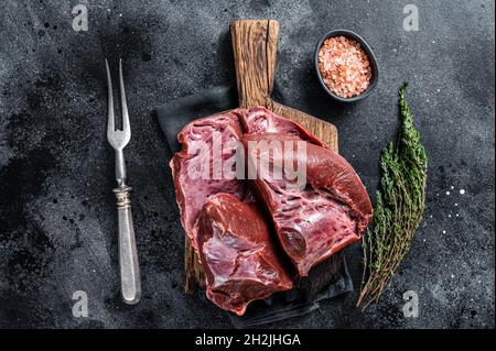 Rohes geschnittes Rind- oder Kalbsherz auf einem Schlachtbrett. Schwarzer Hintergrund. Draufsicht Stockfoto