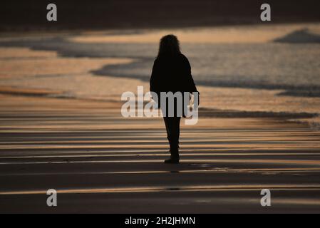 Eine Person, die in der Abenddämmerung an einem Strand in Whitby entlang spazierenierte Stockfoto