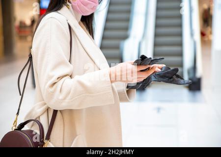 Frau mittleren Alters zieht ihre Handschuhe in der Mall auf Rolltreppe Hintergrund. Gesichtslos Stockfoto