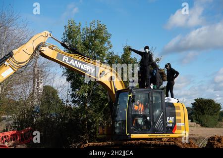 Chalfont St Peter, Großbritannien. Oktober 2021. Stopp HS2-Demonstranten aus dem Kriegslager Wendover aktiver Widerstand besetzten einen Bagger, der heute vor dem Gelände des HS2 Chalfont St Peter Hochwasserschutzarbeiten durchführte, wo die Überschwemmungen auf der Straße angeblich viel schlimmer wurden, seitdem HS2 vor Ort Bäume und Felder geräumt hat. Es wurde berichtet, dass HS2 1,600 Kubikmeter potenziell stark verschmutzenden Bentonits in den Kalkaquifer am Standort verloren hat. Quelle: Maureen McLean/Alamy Live News Stockfoto