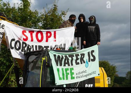 Chalfont St Peter, Großbritannien. Oktober 2021. Stopp HS2-Demonstranten aus dem Kriegslager Wendover aktiver Widerstand besetzten einen Bagger, der heute vor dem Gelände des HS2 Chalfont St Peter Hochwasserschutzarbeiten durchführte, wo die Überschwemmungen auf der Straße angeblich viel schlimmer wurden, seitdem HS2 vor Ort Bäume und Felder geräumt hat. Es wurde berichtet, dass HS2 1,600 Kubikmeter potenziell stark verschmutzenden Bentonits in den Kalkaquifer am Standort verloren hat. Quelle: Maureen McLean/Alamy Live News Stockfoto