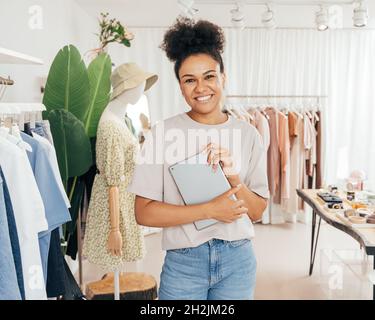 Porträt einer glücklichen Managerin in einem kleinen Modegeschäft, die ein digitales Tablet hält und die Kamera anschaut Stockfoto