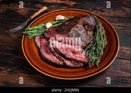Gerösteter Aufhänger oder Onglet-Rinderfleischsteak in Scheiben auf einem rustikalen Teller mit Hackschnitzel. Dunkler Holzhintergrund. Draufsicht Stockfoto