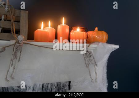 Halloween-Heimtextilien. Plastikspielzeug-Skelette in einer Holzkiste am Kamin vor einer dunkelblauen Wand. Eine Girlande aus Skeletten. Spinnennetz auf der Kommode. Stockfoto