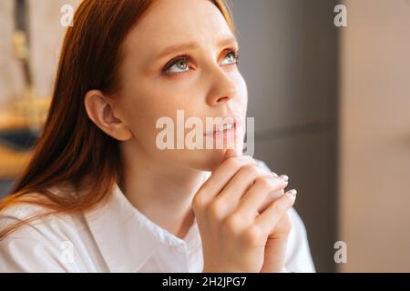 Nahaufnahme des Gesichts einer treuen jungen Frau, die zu Hause die gefalteten Hände vor dem Gesicht hält und nach oben schaut. Stockfoto