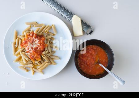 Nudelteller mit Tomate auf weißem Hintergrund. Stück Käse und Reibe. Schüssel mit Tomate. Speicherplatz kopieren. Draufsicht. Stockfoto