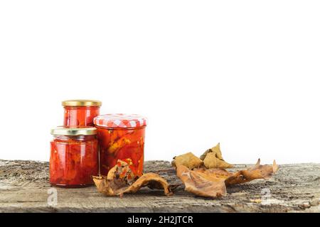 Glasgefäße mit konservierten Paprika auf Holzgrund und weißem Hintergrund mit Herbstlaub Dekoration. Speicherplatz kopieren. Stockfoto