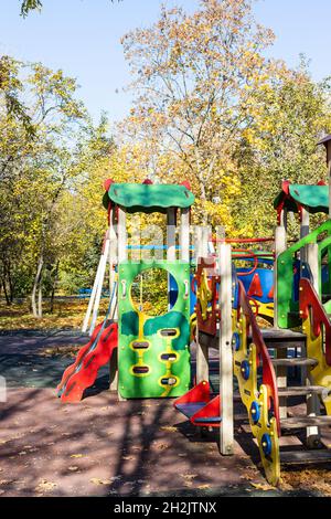 Bunte Holzfahrten, Rutschen und Häuser auf dem Kinderspielplatz im öffentlichen Stadtpark am sonnigen Herbsttag Stockfoto