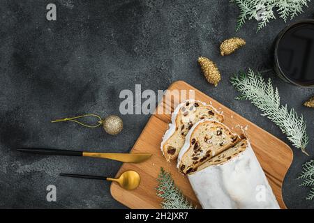 Weihnachtliche Komposition mit Stollenkuchen auf Holzbrett, Kaffeetasse und Besteck auf dunklem Hintergrund. Flach liegend Stockfoto