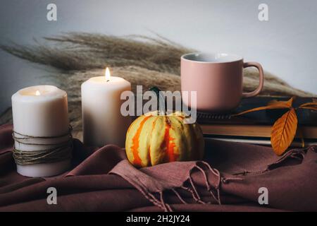 Gelber Kürbis, Kaffeetasse und Kerzen. Stillleben im Herbst. Einrichtung im Boho-Stil. Stockfoto