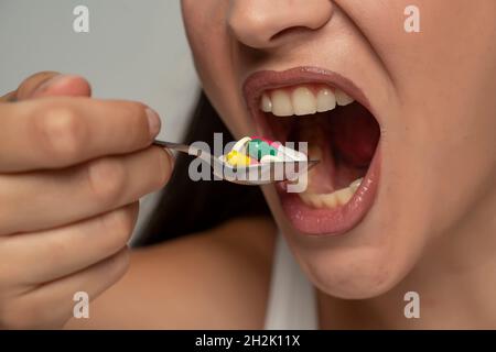 Eine junge Frau legt ihr einen Löffel Medizin in den Mund Stockfoto