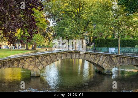 Eine gewölbte Steinbrücke über den Fluss Windrush im malerischen Cotswolds Village in Bourton-on-the-Water, Gloucestershire, England. Stockfoto