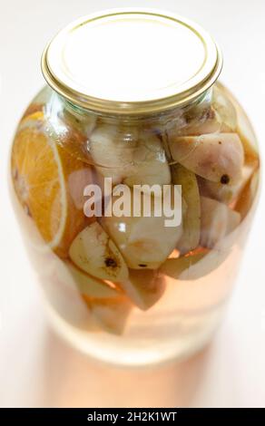 3-Liter-Glas mit hausgemachtem Kompott (geschmortes Obst) aus frisch geschnittenen Äpfeln und Orangen auf hellbraunem Tisch Stockfoto