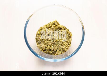 Ansicht von getrockneten zerkleinerten Heilkräutern und Pflanzen in Glasschale auf hellbraunem Tisch Stockfoto
