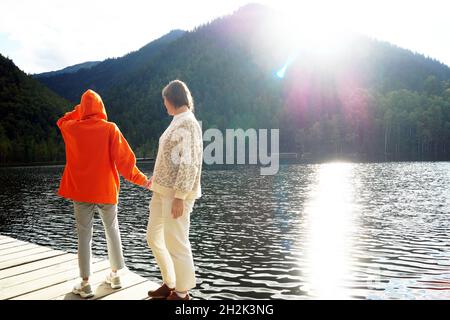 Tochter und Mutter gehen auf einer Holzterrasse auf warmen Seen Stockfoto