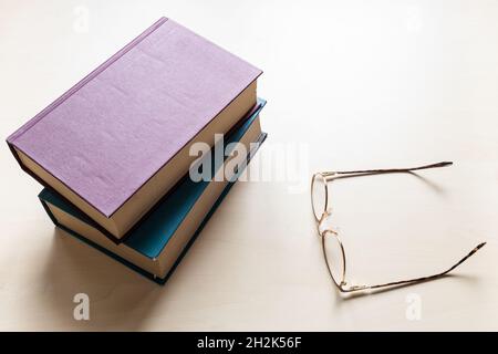 Draufsicht auf Brillen und zwei dicke Bücher auf hellbraunem Holzbrett Stockfoto