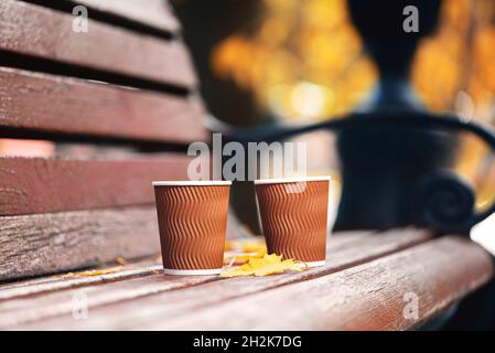 Zwei Pappbecher Kaffee auf einer Holzbank im Herbstpark an sonnigen Tagen. Kaffeezeit Stockfoto