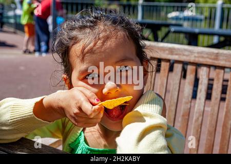 Ein junges englisches/thailändisches Mädchen sitzt auf einer Bank und isst eine Tortilla im Pwllheli Ferienlager Stockfoto