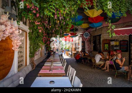 Alacati, Izmir, Türkei - 25 2021. August: Tische in den engen Kopfsteinpflasterstraßen von Alacati warten auf Touristen. Stockfoto