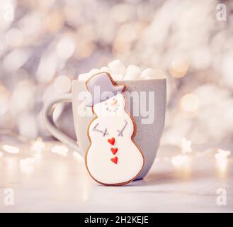 Niedlicher Lebkuchen Schneemann Cookie vor einer Tasse heiße Schokolade mit Marshallows. Hübscher Bokeh-Hintergrund. Stockfoto
