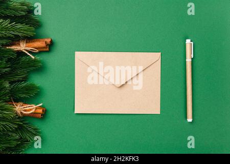 Flache Lay Zusammensetzung aus Bastelpapier Umschlag und Bastelpapier Stift auf grünem isolierten Hintergrund mit Ästen von Weihnachtsbaum und Bündeln von Zimt Stockfoto