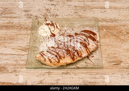 Italienisches Calzone-Dessert mit Creme und Nutella mit Glaszucker auf transparentem Glasplatte und Holztisch Stockfoto