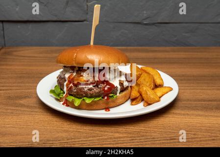 Auf dem Grill gekochter Rinderburger mit viel Mayonnaise, Ketchup, Zwiebeln und Tomaten, garniert mit gebratenen Kartoffelkeilen Stockfoto