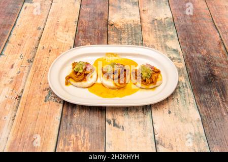 Kleine kolumbianische Maismehl-Arapas mit zerfetztem Fleisch, violetten Zwiebeln und Guacamole Stockfoto