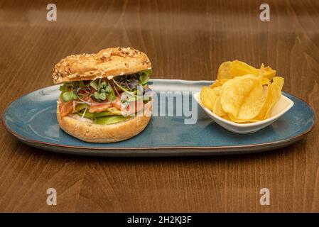 Brotbagel, traditionell aus Weizenmehl, gefüllt mit geräuchertem norwegischen Lachs mit Avocado-Scheiben und verschiedenen Salatsprossen, garniert mit p Stockfoto