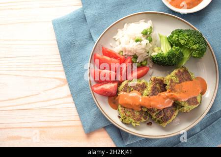 Vegetarische Brokkoli-Patties und Haferflocken mit Tomaten, Reis, Gemüse und würziger Sauce, blauer Serviette und hellem Holztisch, Kopierraum, Draufsicht Stockfoto