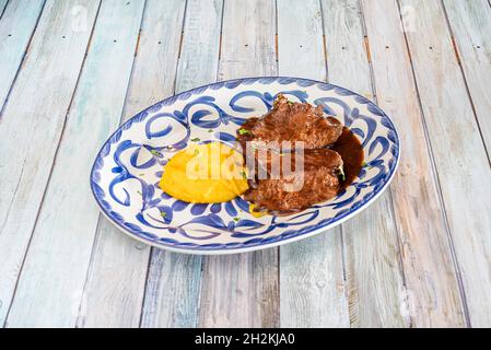 Köstliches spanisches Rezept für Rinderwange in Sauce und Süßkartoffelpüree mit Petersilie auf einem blauen Porzellanteller von Talavera Stockfoto