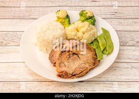 Menüteller mit gebackenem Schweinefleisch, begleitet von weißem Reis, grünen Bohnen, Blumenkohl und gekochtem Brokkoli Stockfoto