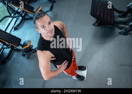 Junge attraktive Athlet männliche Gewicht mit Skala in der Turnhalle und Diät Stockfoto
