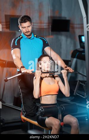 Junge Fitness sportliche weibliche Ausübung Pulldown mit Personal Trainer im Fitnessstudio Stockfoto